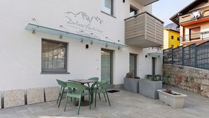 Un patio moderno al aire libre con repisa de vidrio, sillas verdes y pared de piedra.