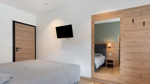 Un dormitorio moderno con una cama, un televisor montado, un espejo y un armario de madera.