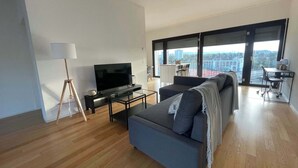 A modern living room with a flat-screen TV, a sofa, a coffee table, and a floor lamp. - Apt near City Center, Novartis & Messe+Basel Card (Basel)