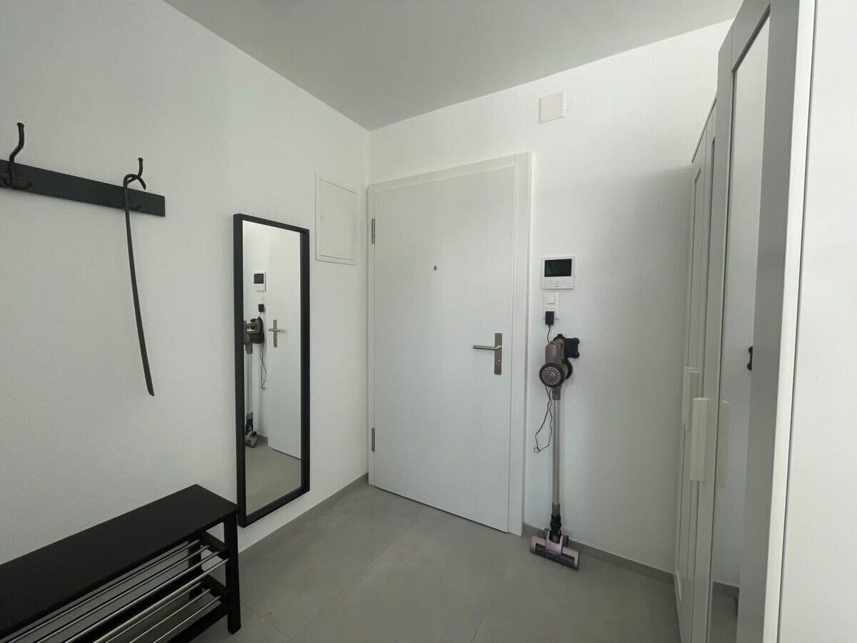 A room with a large mirror, a black bench, a door, and a hairdryer on the floor.