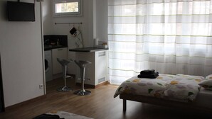 Una habitación de hotel con una cama, dos taburetes altos, una pequeña cocina y una ventana con cortinas.