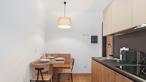 A compact kitchen with wooden cabinets, a dining table with chairs, a hanging light fixture, and a built-in microwave.