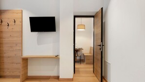 A hallway with a wooden desk, a mounted TV, and a dining area with a hanging light fixture.
