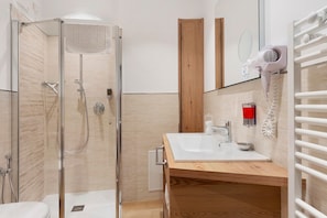 Uma casa de banho moderna com cabine de duche em vidro, toucador de madeira com lavatório e secador de cabelo fixado na parede.
