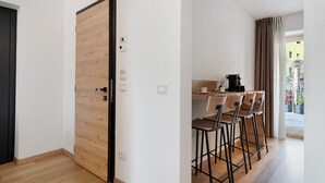 A modern kitchen with a dining area, wooden flooring, and a large window with curtains.