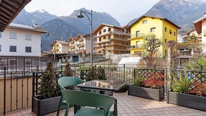 A terrace with a table and chairs, a view of a mountain, and buildings with balconies.