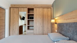 A bedroom with a bed, a wardrobe with a mirror, and a wall-mounted light fixture.