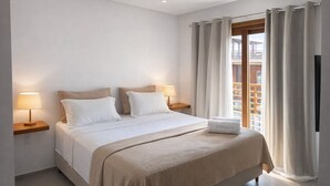 A neatly made bed with white bedding, two bedside lamps, and a small table with a lamp. - Apartamento Messina  (Jijoca de Jericoacoara)