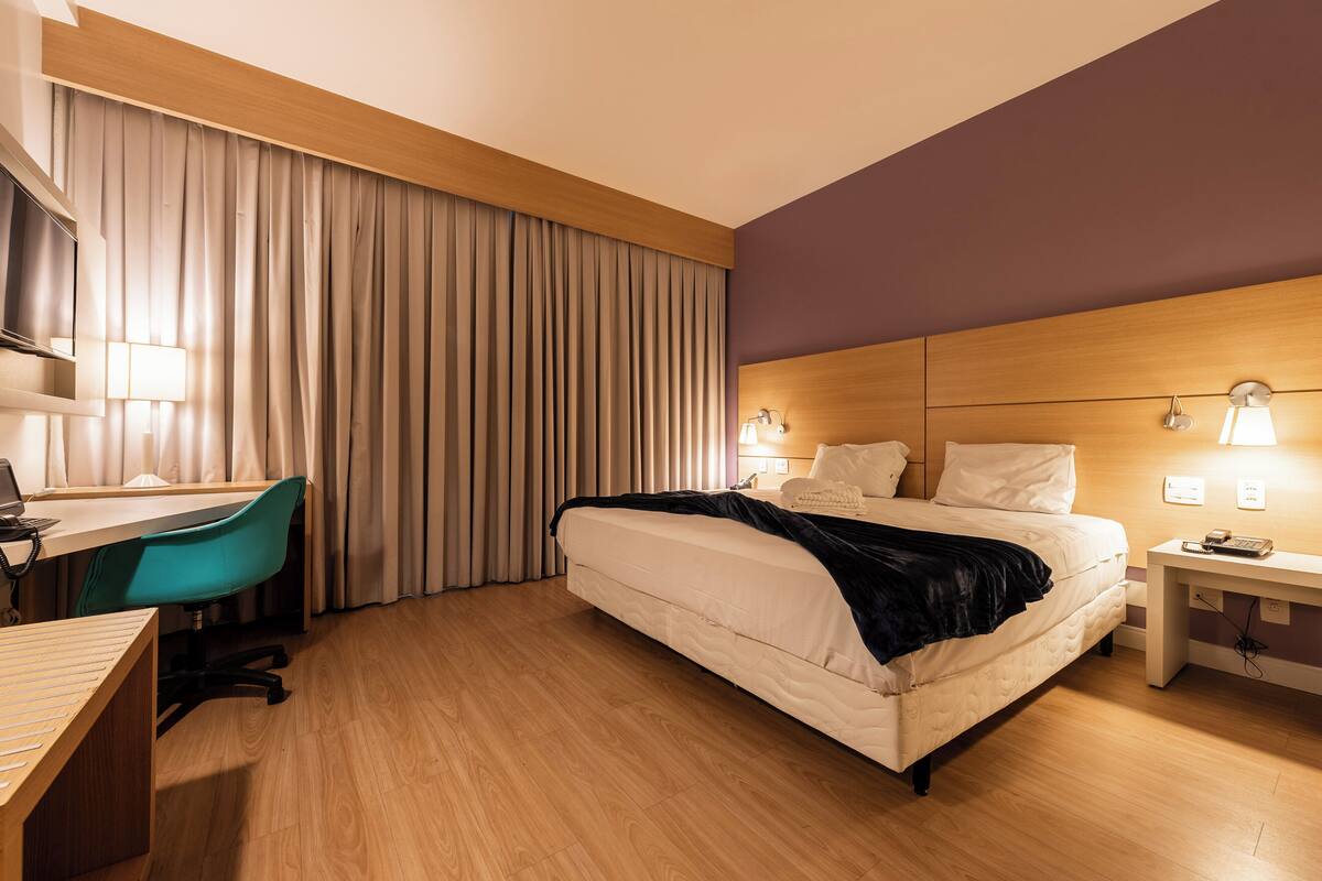A hotel room with a bed, desk, chair, and curtains.