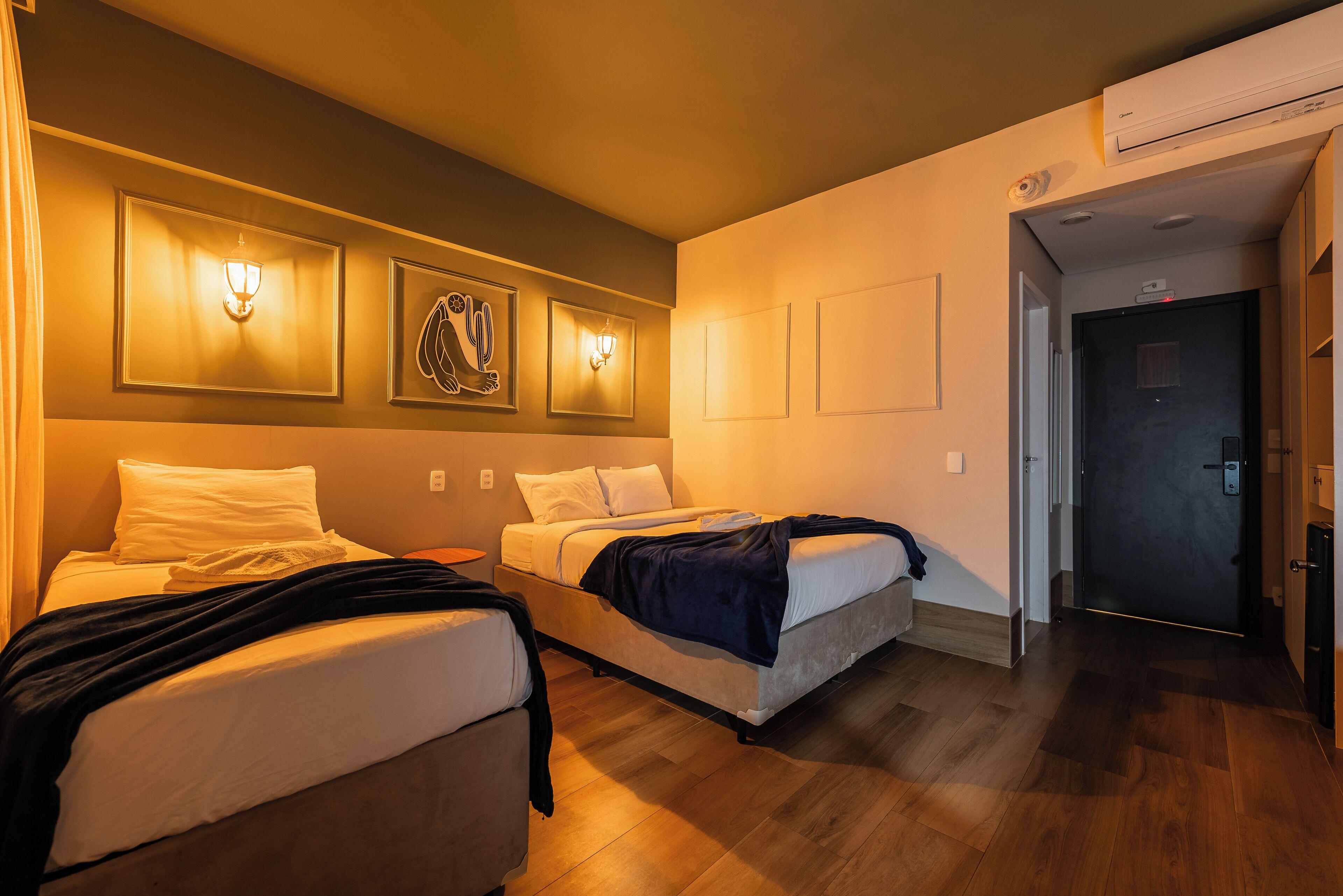 Habitación de hotel con dos camas, aire acondicionado en la pared y una puerta que da a otra habitación.