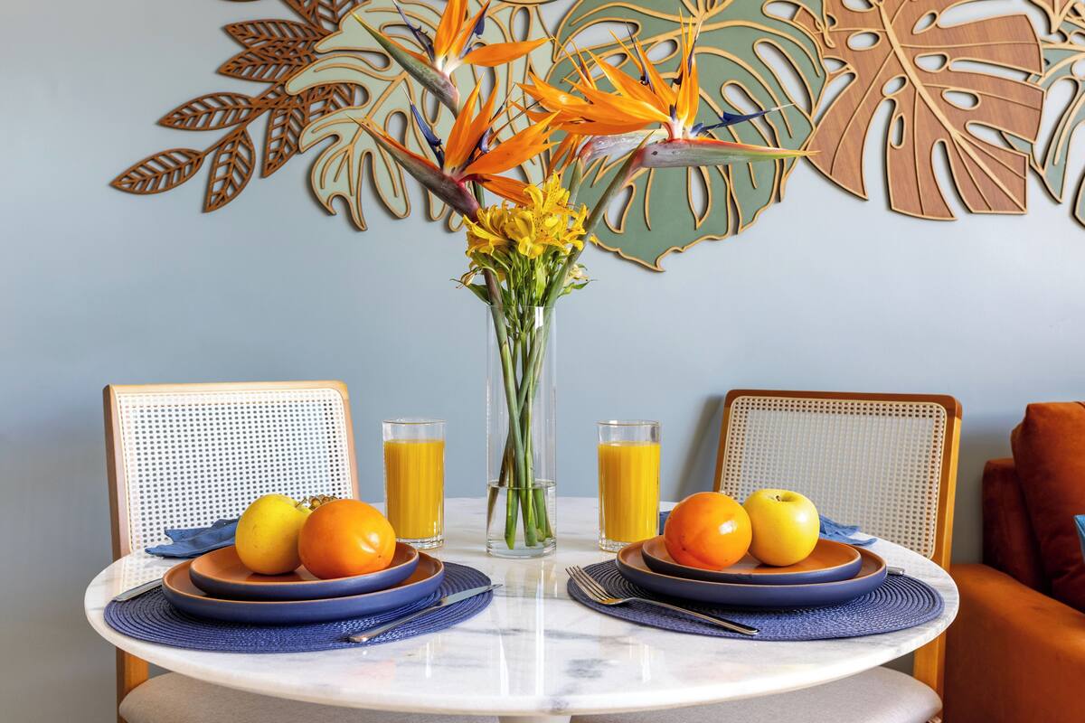 A dining table with two plates of fruit, two glasses of orange juice, and a vase with flowers.