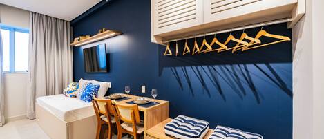 A modern hotel room with a bed, a dining table, and a seating area with cushions.