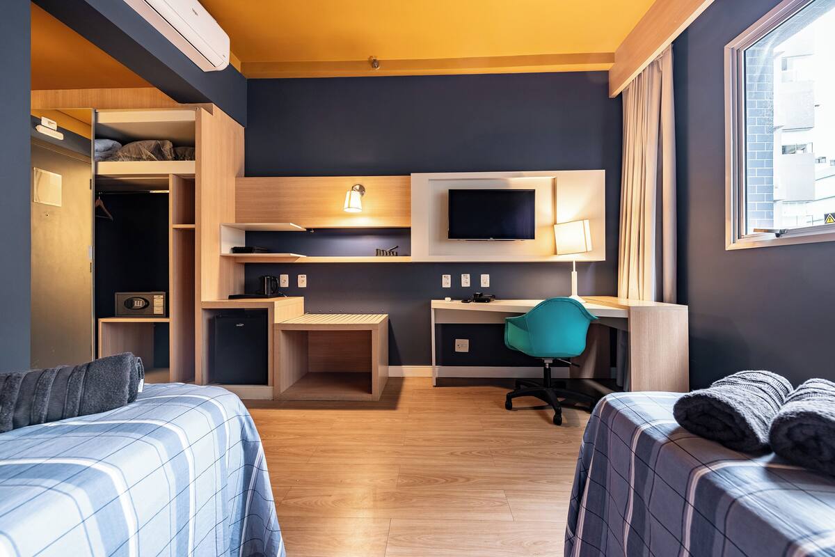 A compact hotel room with a bed, a desk, a chair, a TV, and a wardrobe.