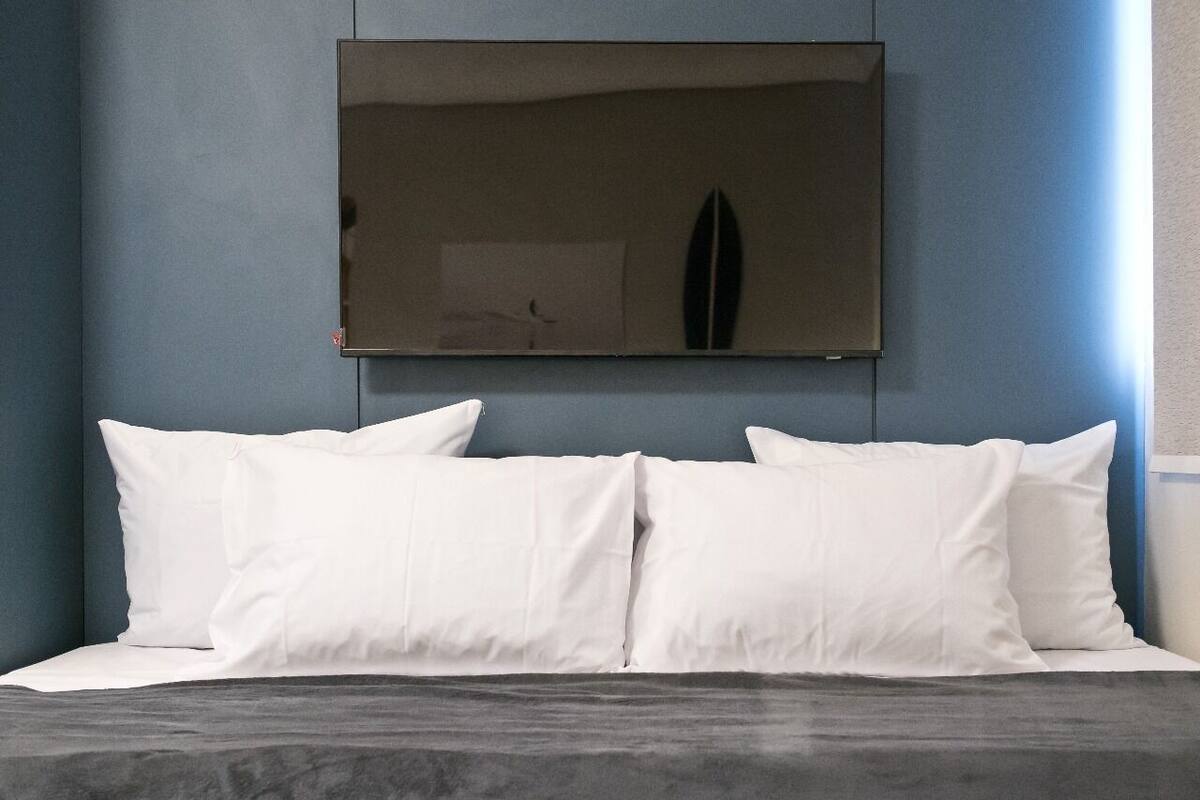 A bed with white pillows and a dark headboard against a blue wall.