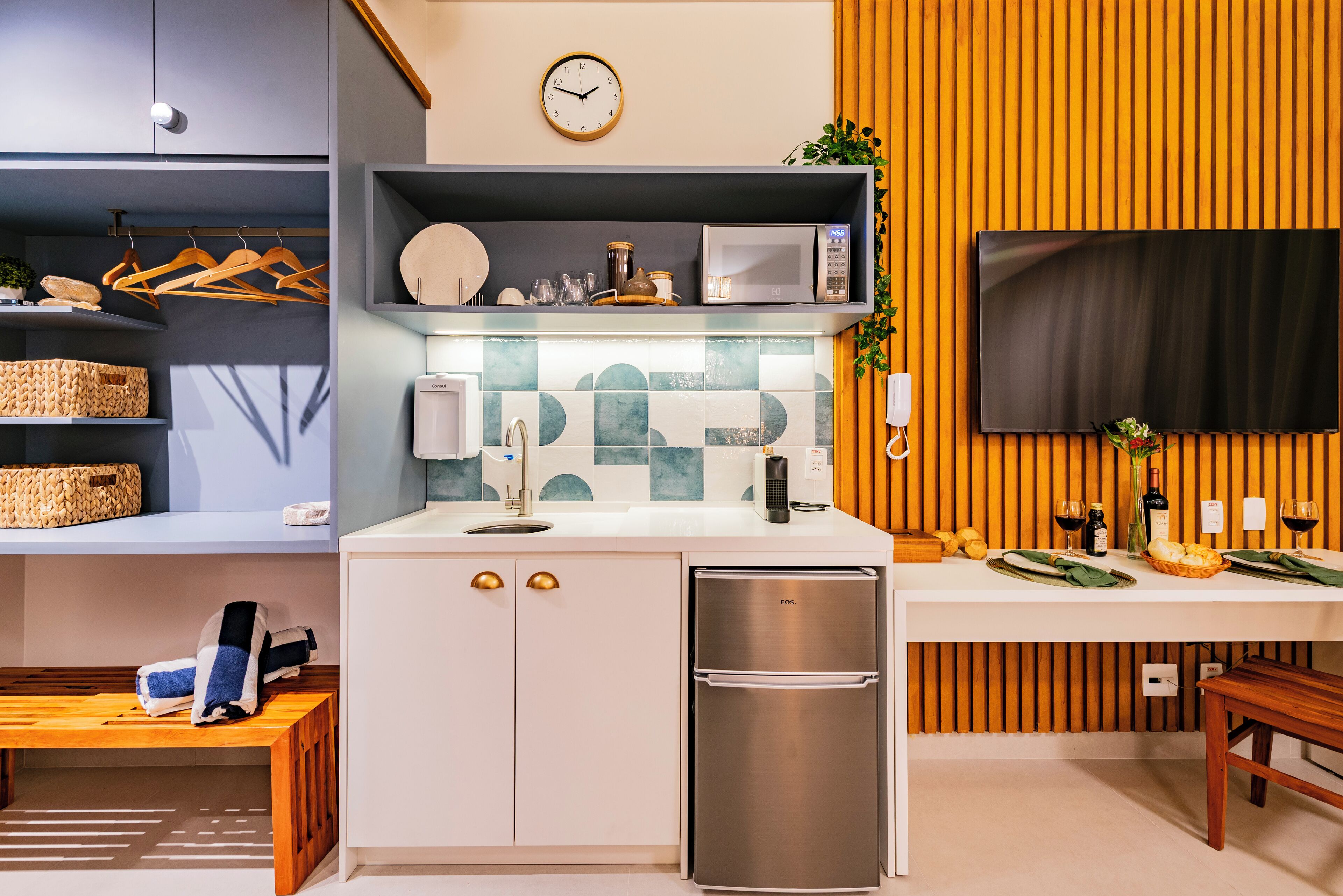 A modern kitchen with a built-in microwave, stainless steel refrigerator, and wooden panel wall.