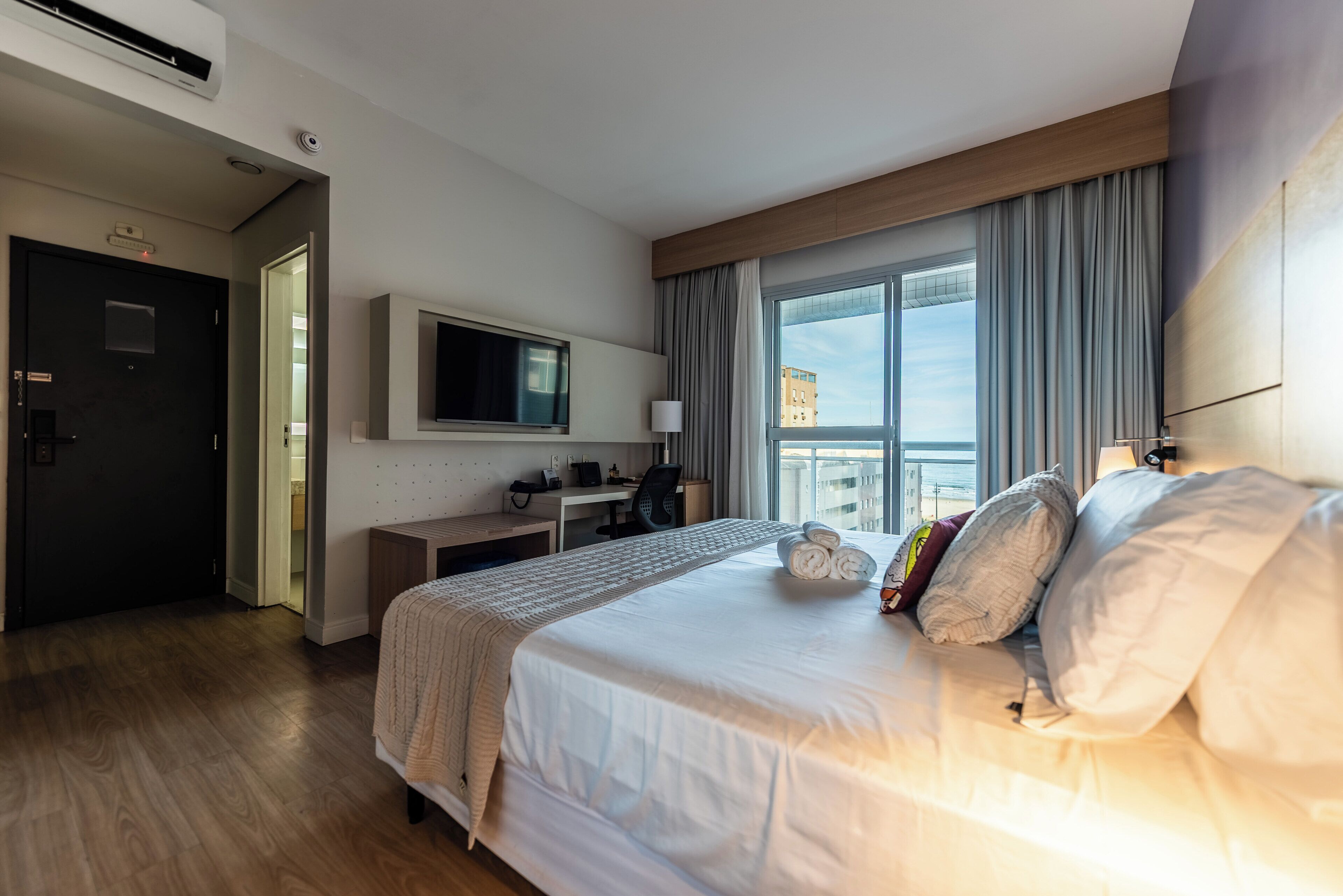 Una habitación de hotel con una cama, un escritorio, un televisor y un ventanal con cortinas.