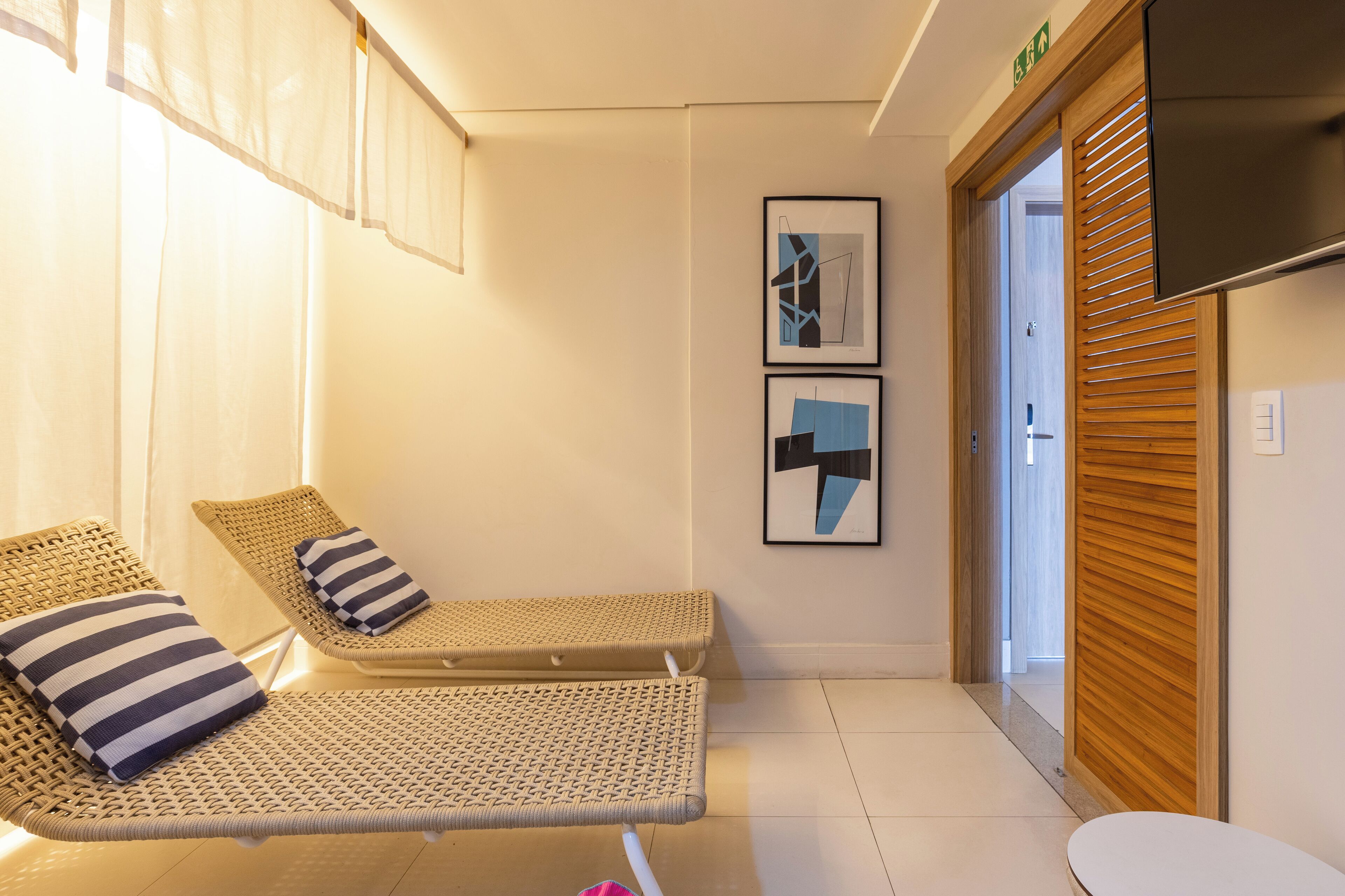 Une pièce comprenant deux fauteuils de relaxation en osier, une petite table blanche et deux œuvres d’art abstraites encadrées accrochées au mur.