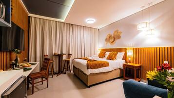 A modern hotel room with a bed, bedside table, chair, and a small dining area with a table and chairs.