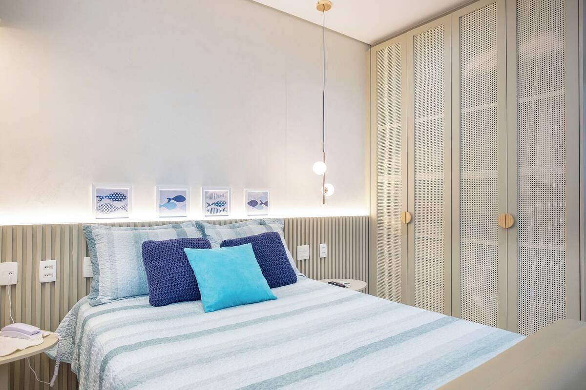 A modern hotel room with a bed, bedside tables, and a wardrobe with a perforated design.