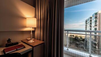 Habitación de hotel con escritorio, lámpara y vistas de la ciudad desde un balcón.