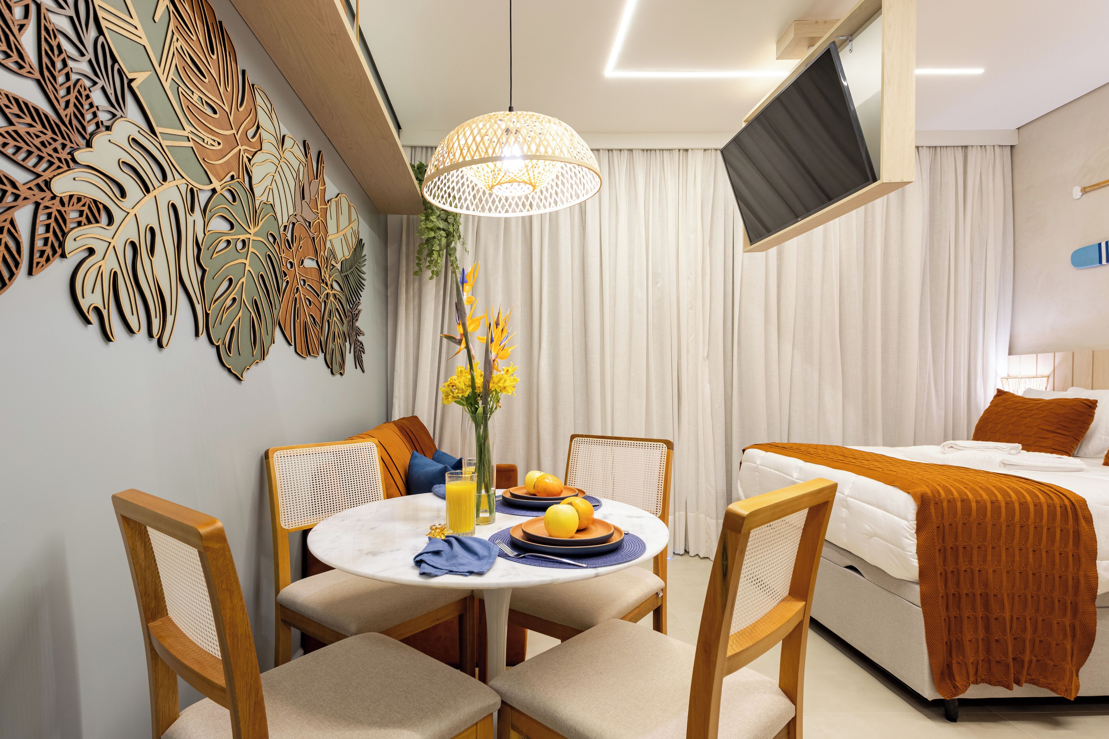 Una habitación de hotel moderna con comedor, una cama con manta marrón y un televisor montado en la pared.