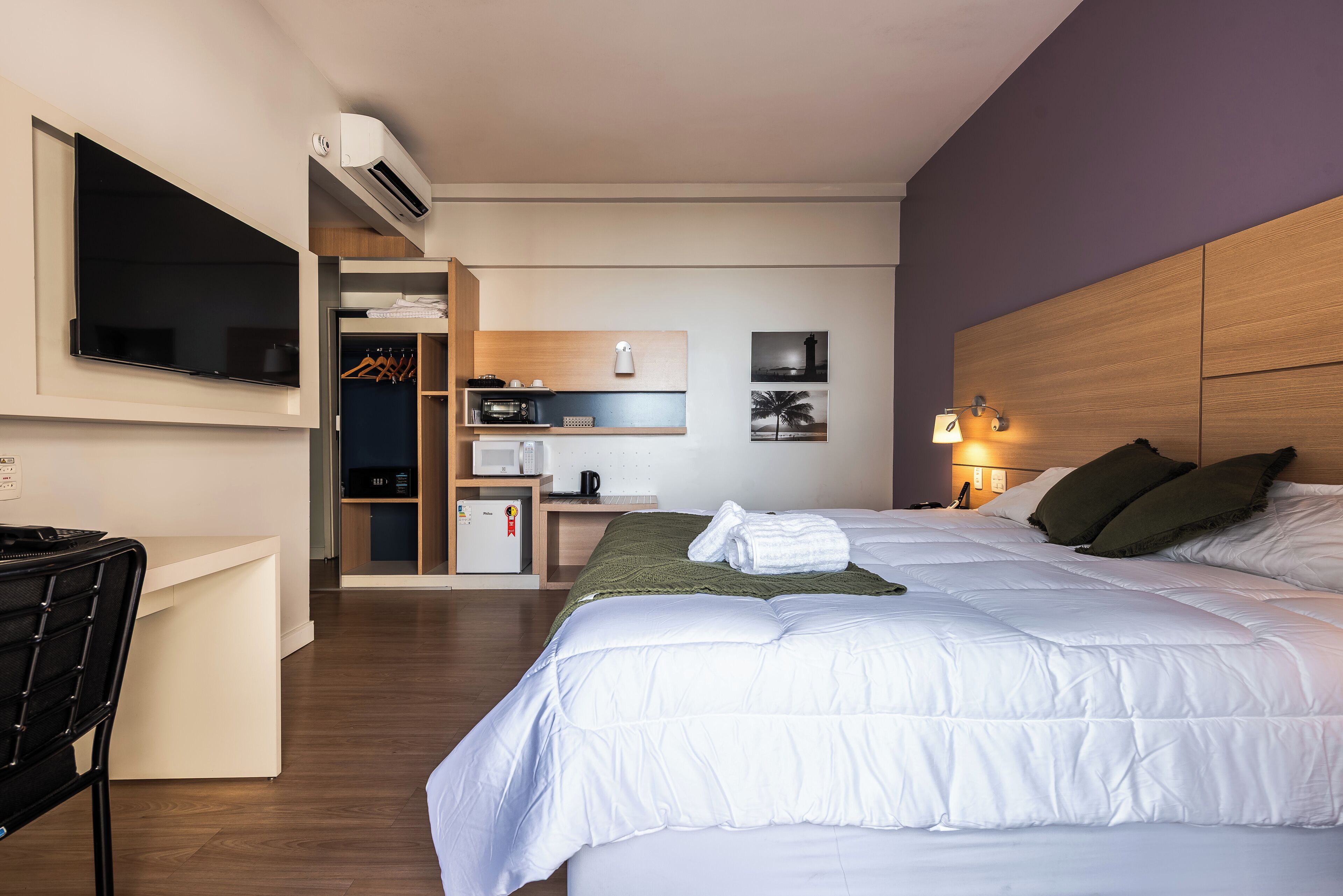 Una habitación de hotel con cama, escritorio, televisión, kitchenette y baño.