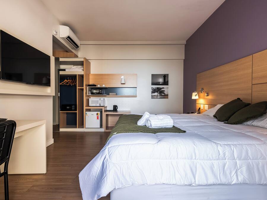 Una habitación de hotel con cama, escritorio, televisión, kitchenette y baño.