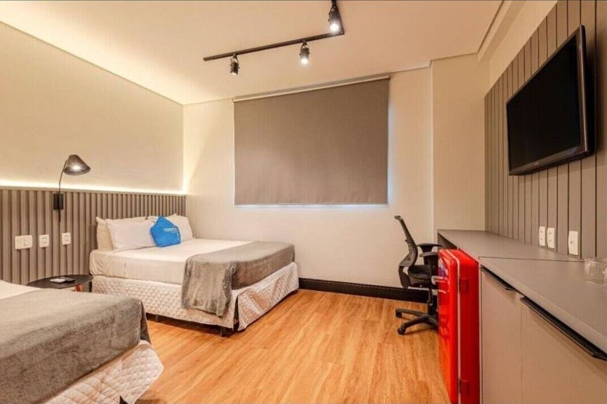 A modern bedroom with a bed, bedside tables, a desk, a chair, a TV, and a window.