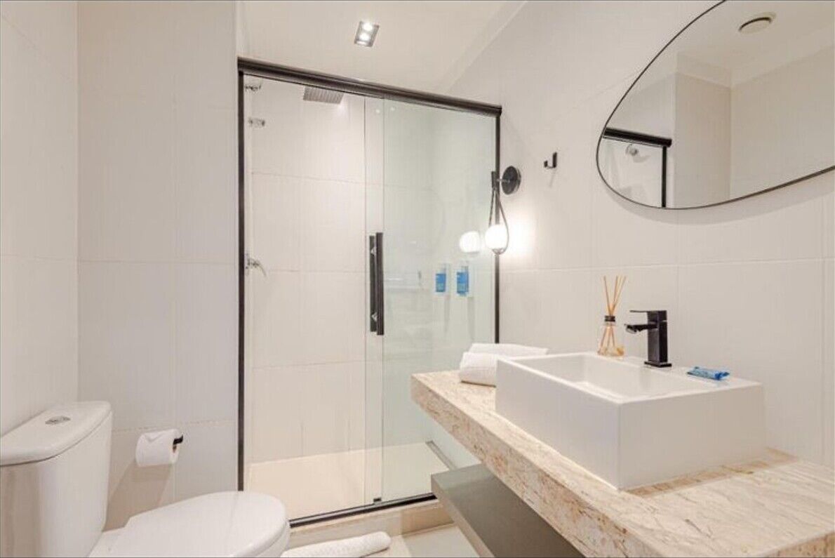 Un baño moderno con cabina de ducha de vidrio, un lavabo blanco y un espejo grande.
