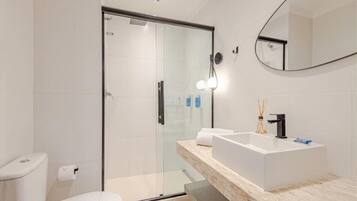 Un baño moderno con cabina de ducha de vidrio, un lavabo blanco y un espejo grande.