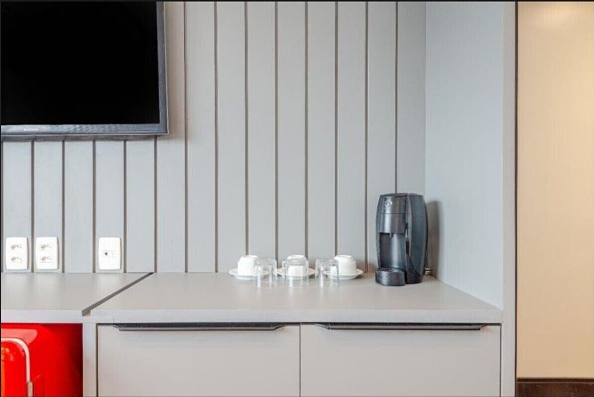 Una kitchenette con cafetera, tazas y un televisor montado en la pared.