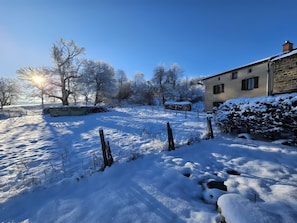 Paesaggio innevato con un edificio in pietra, alberi spogli e cielo sereno.