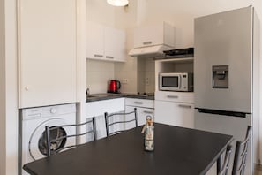 Una cocina compacta con lavadora, microondas, dispensador de agua y una mesa de comedor con sillas.