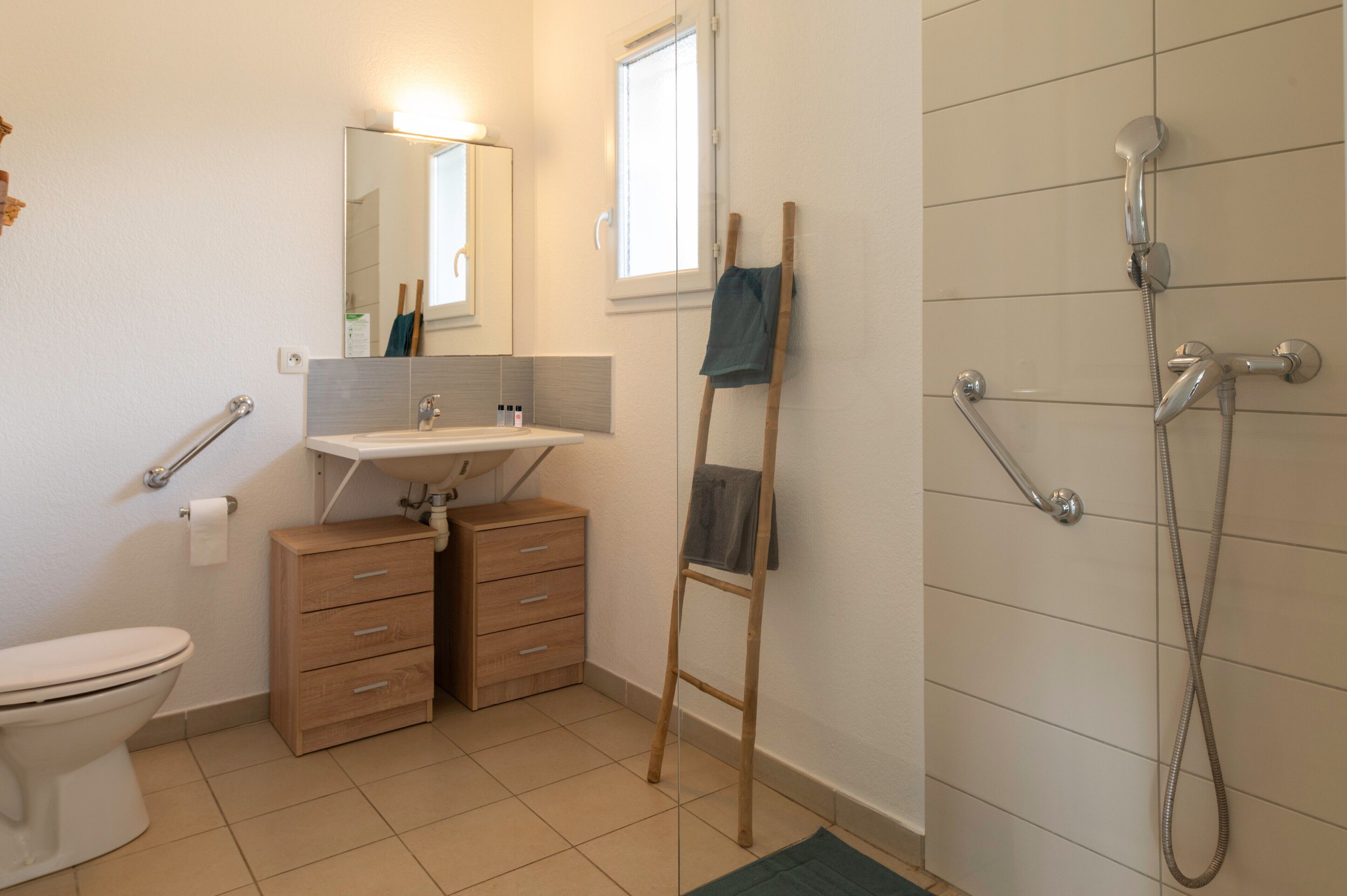 A bathroom with a toilet, sink, wooden cabinet, mirror, and shower.