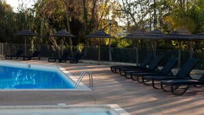 A swimming pool with lounge chairs and umbrellas, surrounded by a fence and trees. - Apartment 'Chez Lena' 100m from the Sea with Shared Pool, Wi-Fi, and Air Conditioning (Poggio-Mezzana)