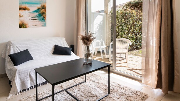 A bedroom with a bed, a bedside table, a window with curtains, and a view of the outdoors. - Apartment 'Chez Lena' 100m from the Sea with Shared Pool, Wi-Fi, and Air Conditioning (Poggio-Mezzana)