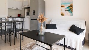 A modern kitchen with white cabinets, a grey refrigerator, and a dining area with a black table and chairs. - Apartment 'Chez Lena' 100m from the Sea with Shared Pool, Wi-Fi, and Air Conditioning (Poggio-Mezzana)