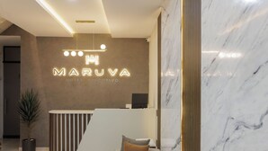 A modern hotel reception area with a marble wall, a reception desk, a sofa, and a potted plant. - MARUVA Hotel Ejecutivo (Tecomán)