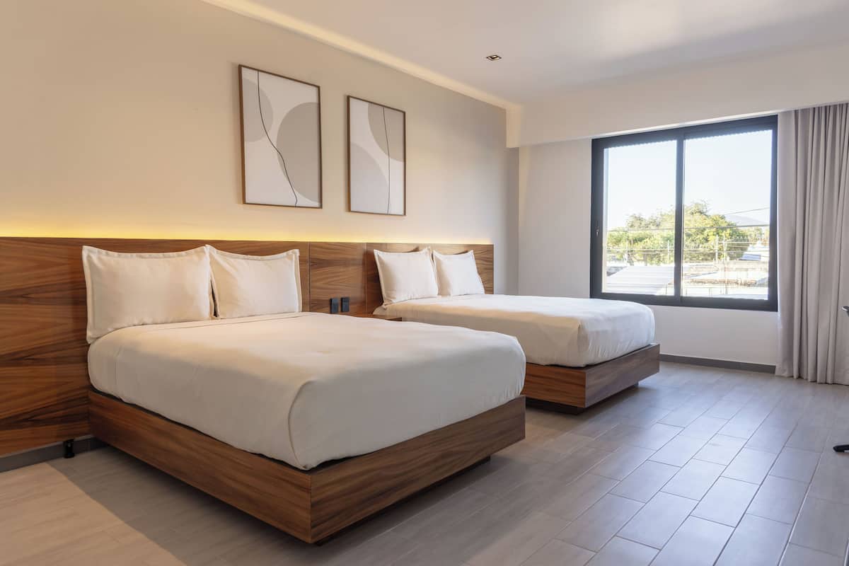 Ein Hotelzimmer mit zwei Betten, Holz-Kopfteilen und großen Fenstern mit Vorhängen.