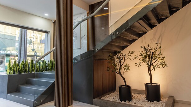 A modern staircase with glass railings and a wooden accent column, leading to an upper floor. - MARUVA Hotel Ejecutivo (Tecomán)