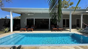 A modern outdoor pool area with a covered patio, lounge chairs, and a view of the house. - Montezuma Jungle House with Pool + Sunset Deck (Montezuma)