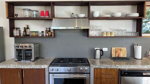 Eine Küche mit Granit Arbeitsplatten, einem Gasherd, einem Backofen, einem Geschirrspüler und Regalen mit Küchenutensilien und Gewürzen.