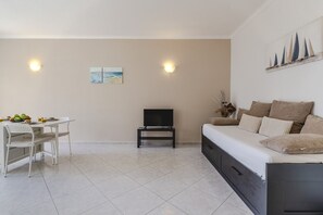 Un salon moderne comprenant un canapé, une table à manger avec des chaises, un téléviseur posé sur un meuble et des œuvres d’art accrochées aux murs.