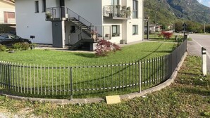 A modern two-story house with a staircase, a small balcony, and a well-maintained lawn. - Meraki Dolomites - Cozy Apartment with Garden and Mountain View (Longarone)