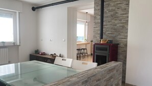 A modern kitchen with a glass dining table, stone wall, and a built-in oven. - Meraki Dolomites - Cozy Apartment with Garden and Mountain View (Longarone)