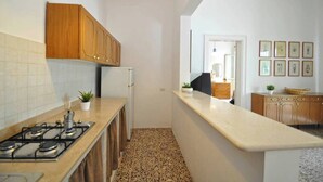 A narrow kitchen with a gas stove, wooden cabinets, and a tiled backsplash. - Villetta Macao 2 in Torre Suda (Racale)