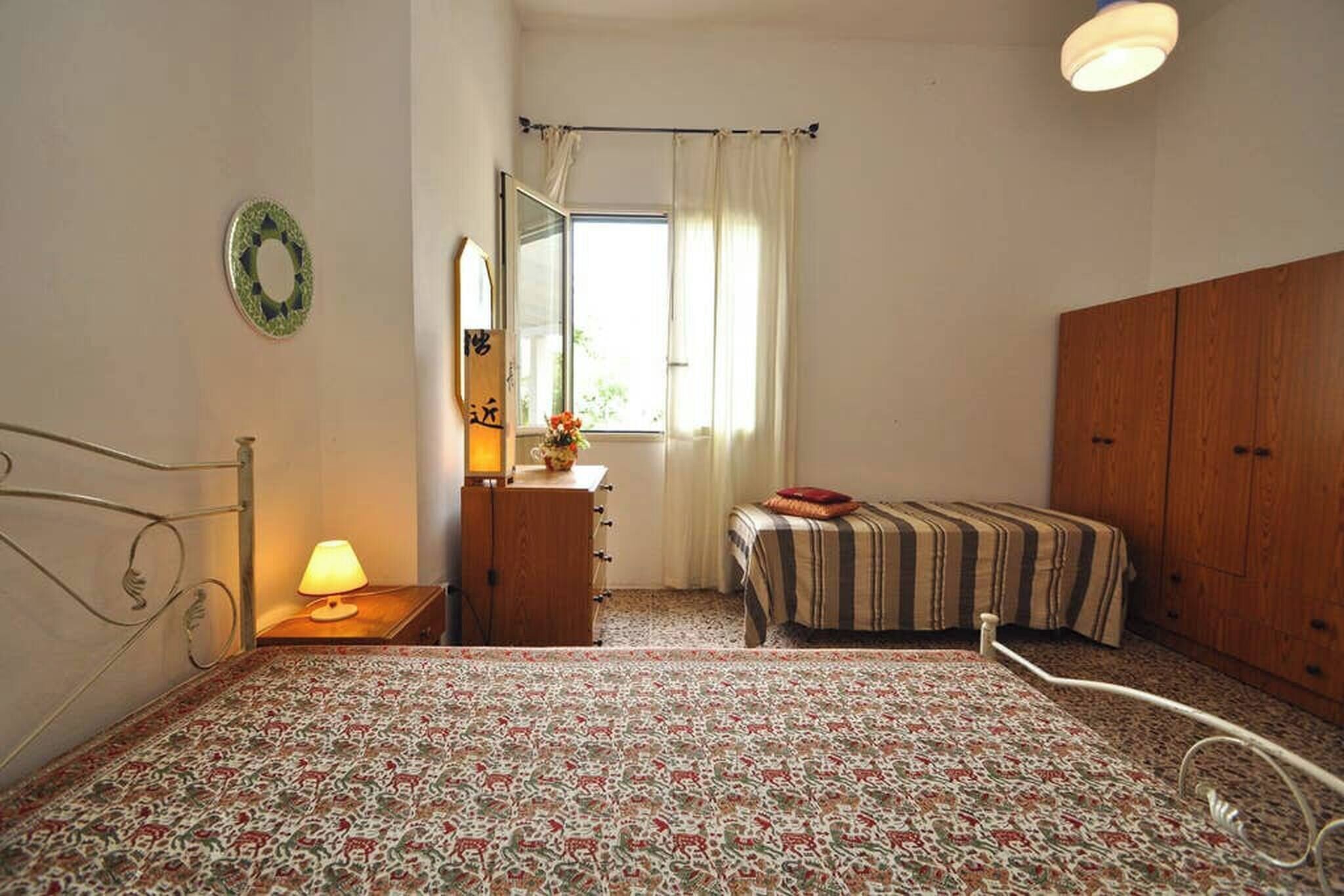 A bedroom with a bed, a dresser, a mirror, a window with curtains, and a wardrobe.