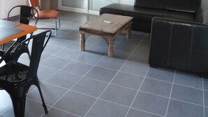 Ein Wohnzimmer mit Holzboden, einem schwarzen Sofa, einem Holztisch, einem Fernseher auf einem Schrank und einer Glastür zum Balkon.