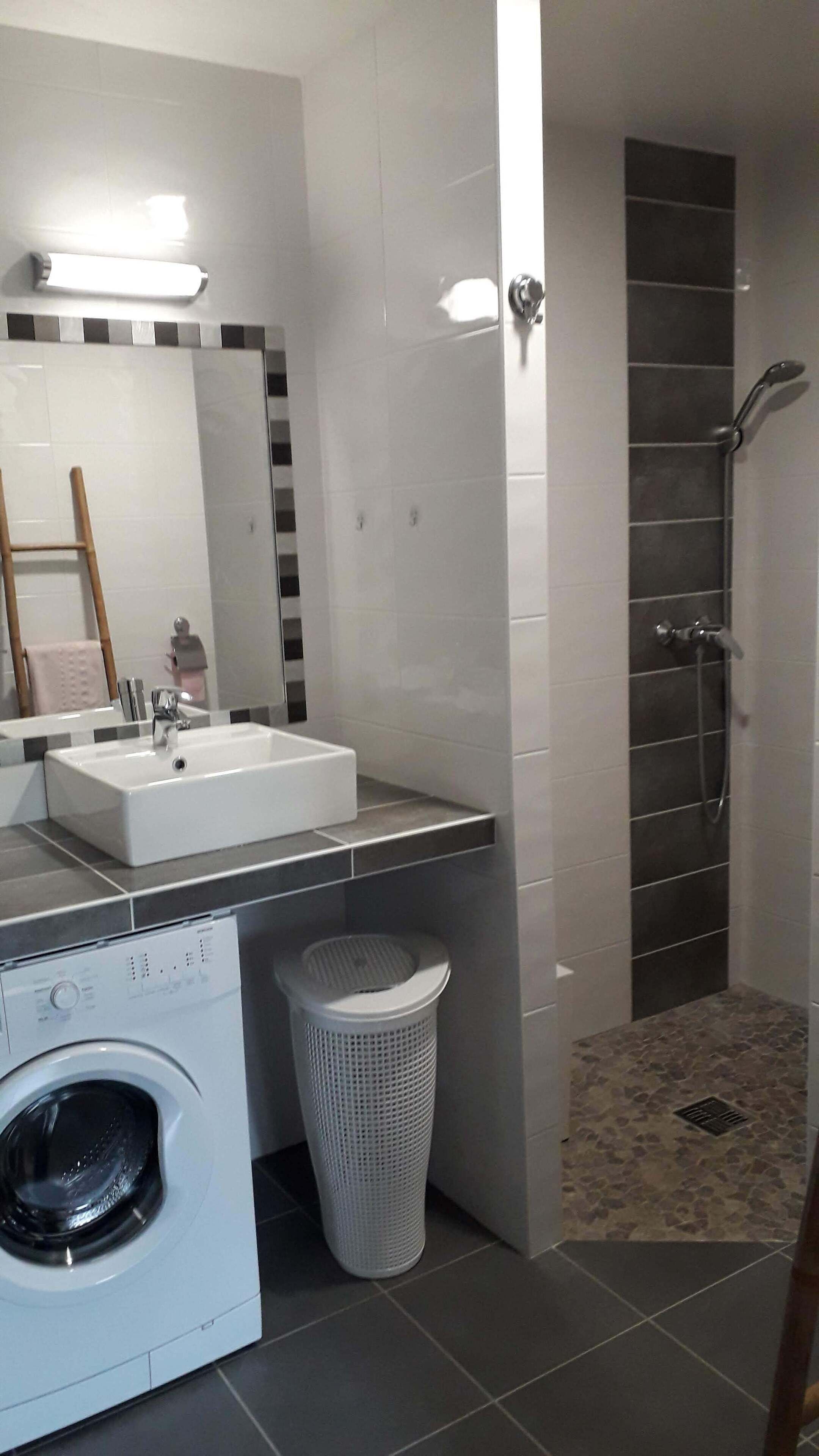 Une salle de bain moderne avec un lavabo blanc, un miroir et un espace douche.