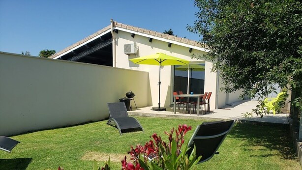 Ein Garten mit Rasen, einem Grill, einem Esstisch mit Stühlen und einem gelben Sonnenschirm.
